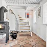 Raum mit Kaminofen, Treppe und Fenster. Boden aus Terrakottafliesen.