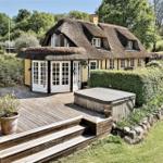 Haus mit Strohdach, Holzterrasse und Whirlpool im Garten.