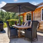 Terrasse mit Tisch, Stühlen und Sonnenschutz neben Holzhäusern.