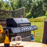 Außenbereich mit Grill, Tisch, Stühlen und Blumen. Hintergrund: grüner Garten.