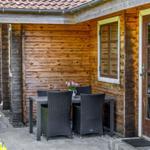 Terrasse mit Tisch und Stühlen neben Holzhaus mit Fenster und Tür.