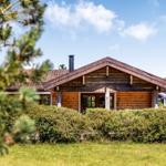 Holzhaus mit Dach und Schornstein hinter Hecke und Bäumen