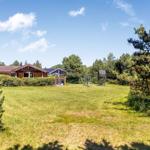 Holzhäuser mit großem Garten und Spielplatz unter blauem Himmel.