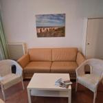 Ein Wohnzimmer mit Sofa, zwei Stühlen und Tisch. Wandbild und Gardinen sind sichtbar.