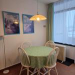 Rundtisch mit vier Stühlen, grüne Tischdecke, Fenster mit Vorhängen.