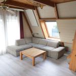 Wohnraum mit Sofa, Tisch und Holzdecke. Fenster und Treppe sind sichtbar.