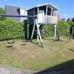 Hinterhof mit Schaukel und Klettergerüst. Grünfläche und Beerenhecke.