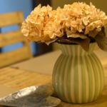 Auf dem Tisch steht eine grün-weiß gestreifte Vase mit getrockneten Hortensien.