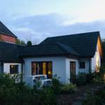 Ein weißes Haus mit schwarzem Dach und beleuchteten Fenstern in einem grünen Garten.