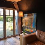 Ein Raum mit braunem Sofa, großer Fensterfront und abstraktem Wandbild.