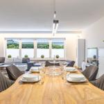 Essbereich mit Holztisch und Stühlen, dahinter Wohnzimmer mit Sofa und Fenster.