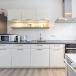 Moderne Küche mit weißen Schränken, Edelstahlgeräten und dunklem Arbeitsplatz.