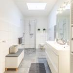 Badezimmer mit Dusche, Waschbecken und Toilette. Weiße Fliesen und graue Bodenfliesen.