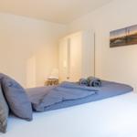 Schlafzimmer mit Bett, Kleiderständer und Wandbild.