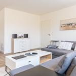 Wohnzimmer mit grauem Sofa, weißen Möbeln und Wandbild.
