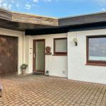 Haus mit weißen Wänden, braunen Fensterrahmen und Garage. Vorgarten mit Pflanzen und Steinplatten.