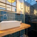 Badezimmer mit Waschbecken auf Holz, blauen Fliesen und Spiegel.