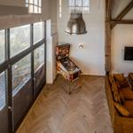 Wohnraum mit Holzboden, Sofa, Pinball und großen Fenstern.