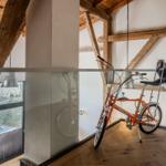 Ein orangefarbener Fahrrad steht in einem Raum mit Holzdecken und Glasgeländer.