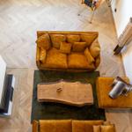 Zwei goldfarbene Sofas, ein Holztisch und ein Pinballautomat auf hellem Parkettboden.