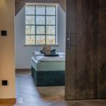 Schlafzimmer mit Bett, Holztür und Fenster mit Blick nach draußen.