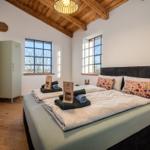 Schlafzimmer mit Doppelbett, Holzboden und zwei Fenstern. Wandmontierte TV und Kleiderschrank.