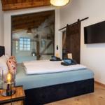 Schlafzimmer mit Bett, Fernseher und Holzboden. Große Glaswand und hölzerne Tür.