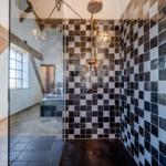 Dusche mit schwarz-weißen Fliesen und Glaswand. Im Hintergrund ein Bett und Fenster.