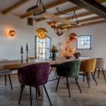 Esszimmer mit Holztisch, bunten Stühlen und hängenden Lampen.