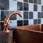 Kupferfarbener Wasserhahn und Waschbecken vor schwarz-weißem Fliesenspiegel.