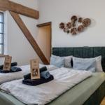 Doppelbett mit grünem Kopfteil, Holzbalken und Fenster mit Blick.