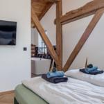 Zwei Betten mit Handtüchern, Holzbalken, Badewanne und Fenster.