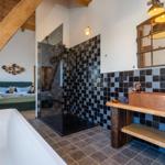 Badezimmer mit Dusche, Badewanne und Waschtisch. Holzdecken und Fliesenwand.