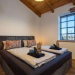 Schlafzimmer mit Doppelbett, Holzbalkendecke und großem Fenster.