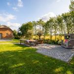 Haus mit strohgedecktem Dach, Terrasse mit Tisch, Bänken und Sitzmöbeln im Garten.