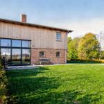 Haus mit Holzfassade und Backsteinbasis, großes Fenster, Garten und Bänke.