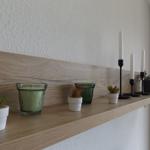 Wooden shelf with plants, candles, and glasses on the wall