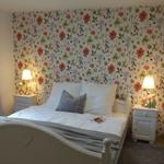 Bedroom with floral wallpaper, white bed, and nightstands with lamps.