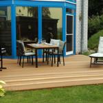Deck with table, chairs, and lounge chair in front of blue house with glass facade.