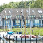 A house with blue windows and balcony, surrounded by boats and grass.