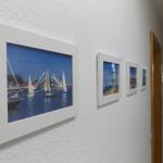 Wall with four framed pictures of sailboats and coastal landscapes.