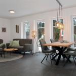 Wohn- und Essbereich mit Sofa, Sessel, Tisch und Stühlen. Fenster und Tür zu Garten.