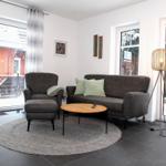 Wohnzimmer mit Sofa, Sessel und runden Teppich. Große Fenster mit Blick nach draußen.