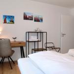 Schlafzimmer mit Bett, Schreibtisch und Wandbildern.