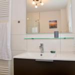 Badezimmer mit Waschbecken, Spiegel und Handtuchhalter.