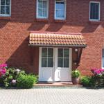 Rotes Backsteinhaus mit weißer Eingangstür und blühenden Pflanzen vor dem Eingang.