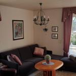 Wohnzimmer mit Sofa, Sessel und Tisch. Fenster mit Vorhängen und Blick auf Terrasse.