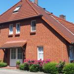 Rotes Backsteingebäude mit Dachgauben und blühenden Sträuchern vor der Tür.