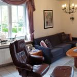 Wohnzimmer mit Sofa, Ledersessel und Glasvitrine. Blick auf Garten durch Fenster.