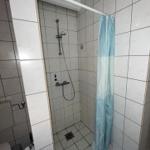 Shower with showerhead, shower curtain, and toilet in a bathroom.